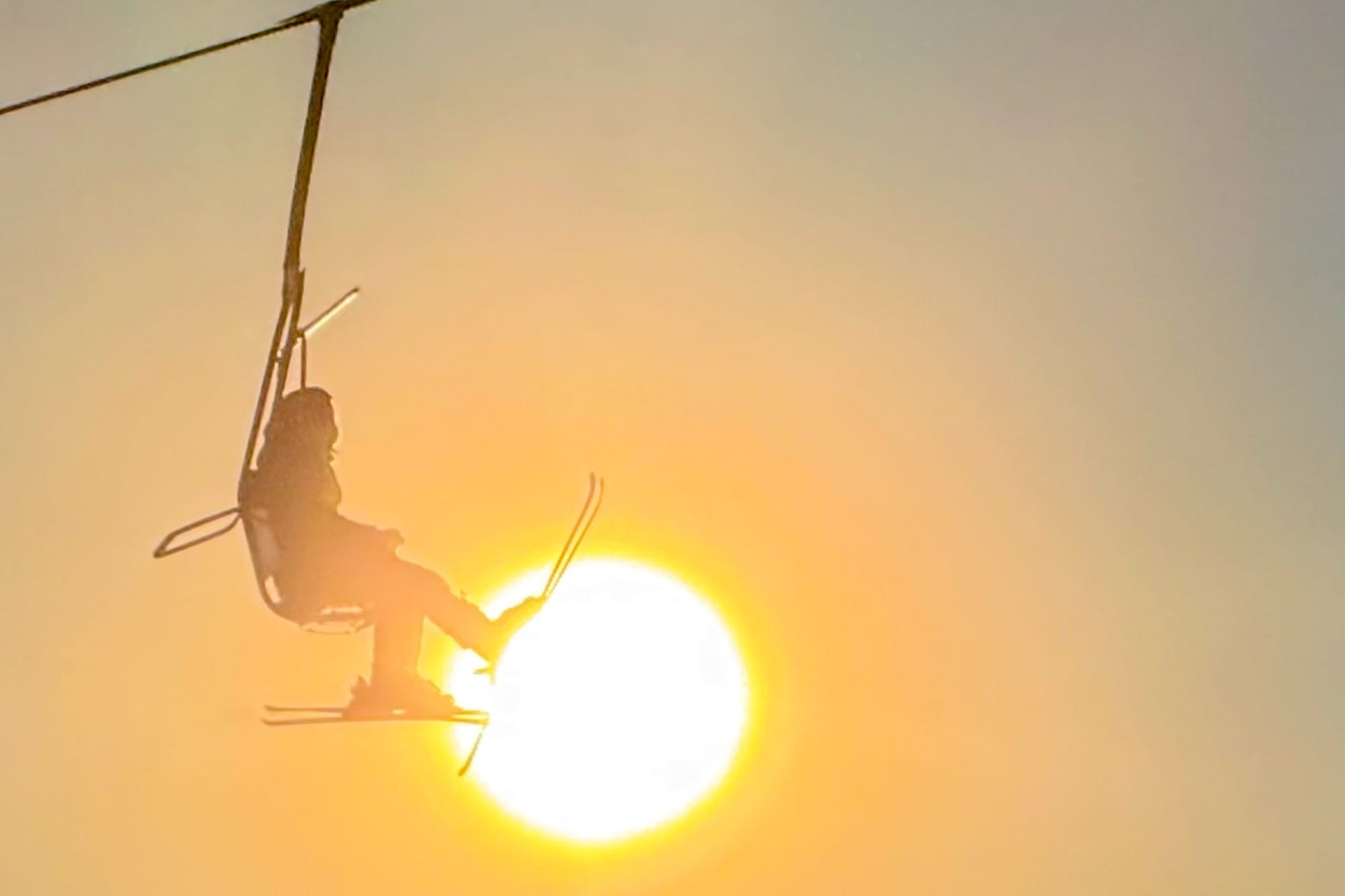 Riders pass in front of the sun while taking the lift at Skeetawk ski area in Hatcher Pass