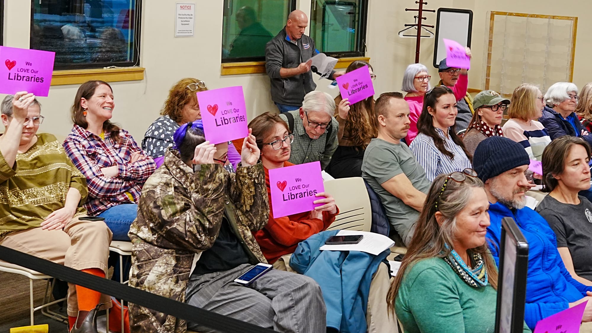 Residents hold up signs during public comment at the Matanuska-Susitna Borough Assembly meeting