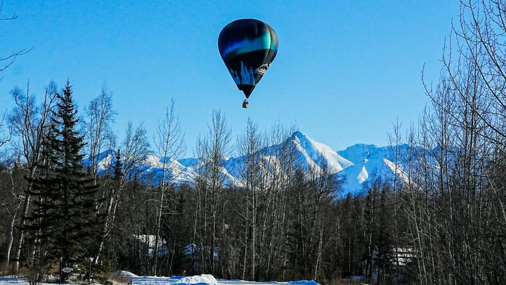 Alaska Helicopter Tour's hot air balloon floats above a neighborhood off 49th State Street
