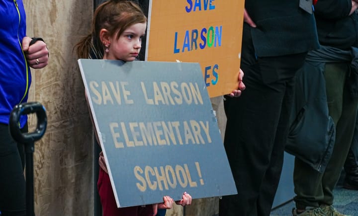 A child holds a "Save Laarson Elementary School" sigh at the Matanuska-Susitna School District School Board meeting